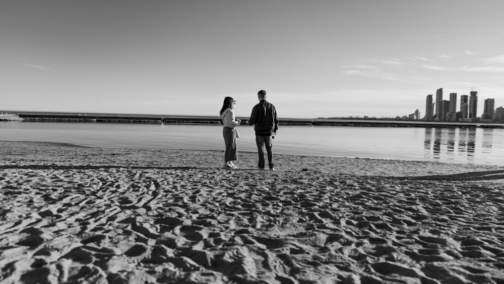 a man and woman standing on a beach next to a body of water