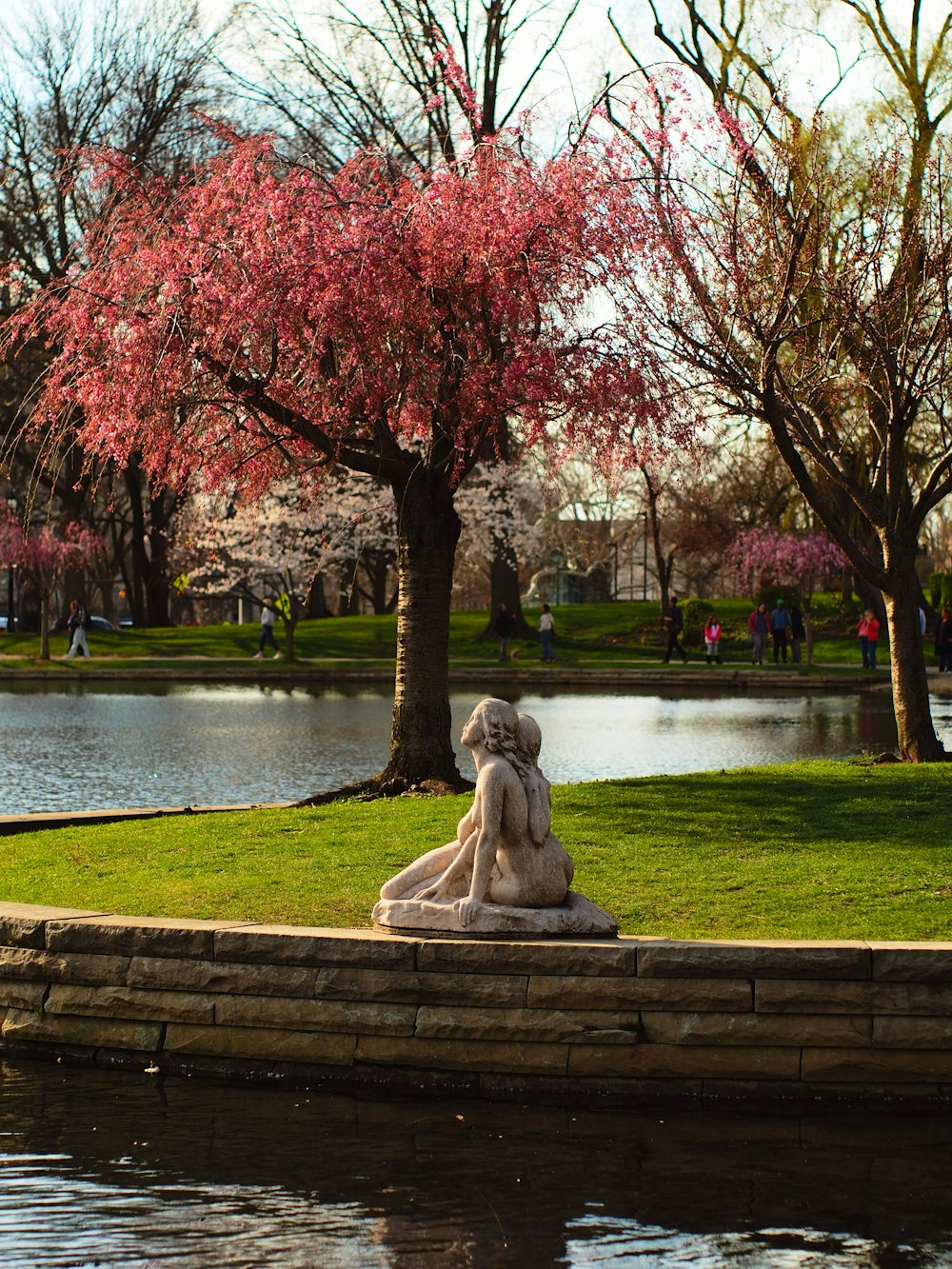 Eine Statue einer Frau, die auf einer Steinmauer neben einem Teich sitzt
