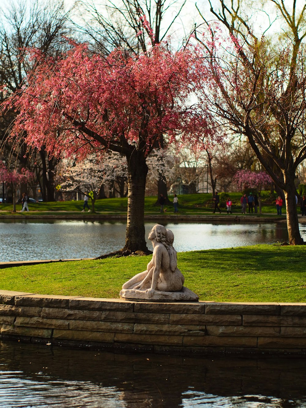 a statue of a woman sitting on top of a stone wall next to a pond