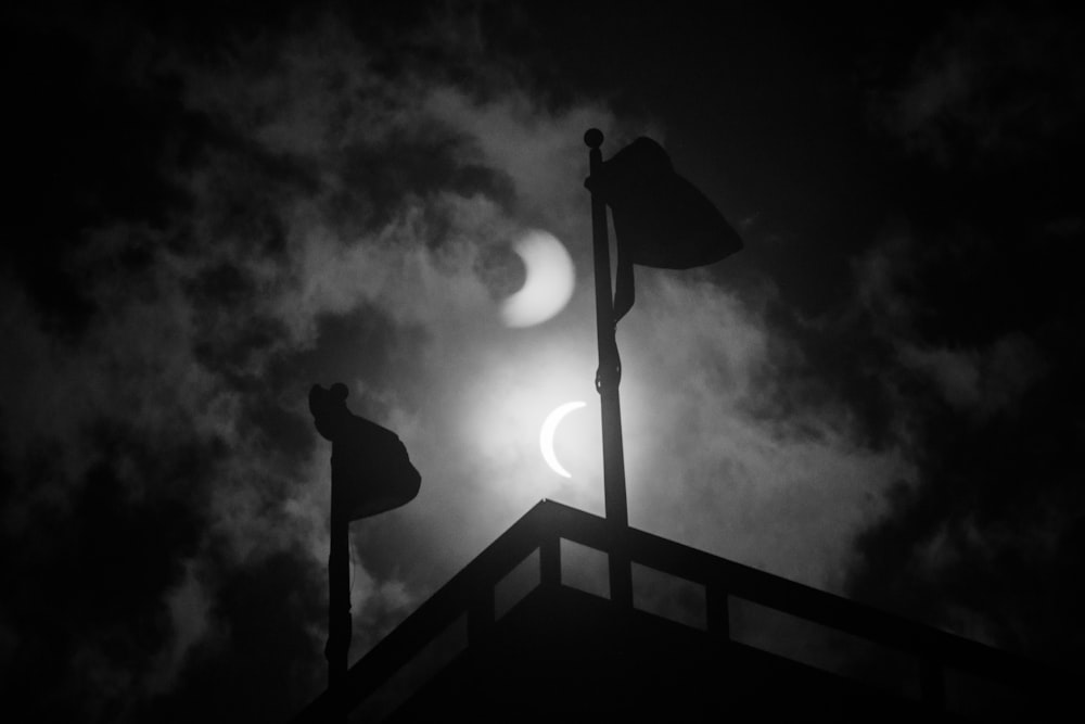 the moon is seen through the clouds behind a weather vane