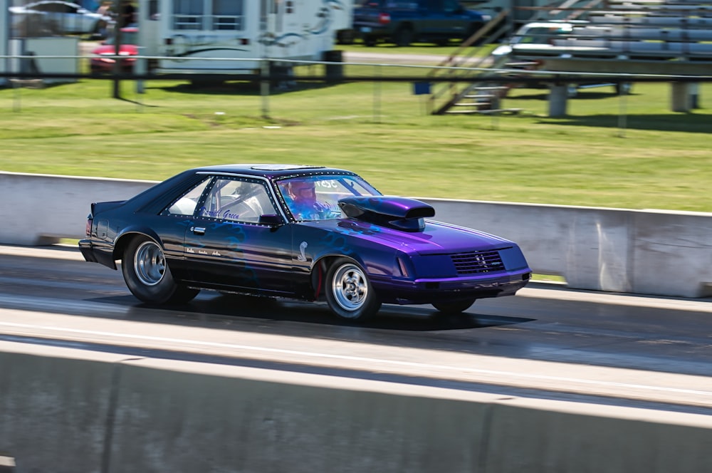 a purple car driving down a street next to a grass covered field