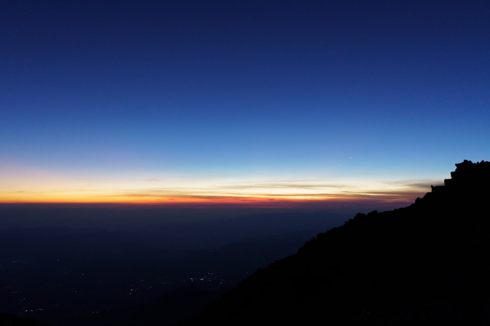 eine Person, die bei Sonnenuntergang auf dem Gipfel eines Berges steht