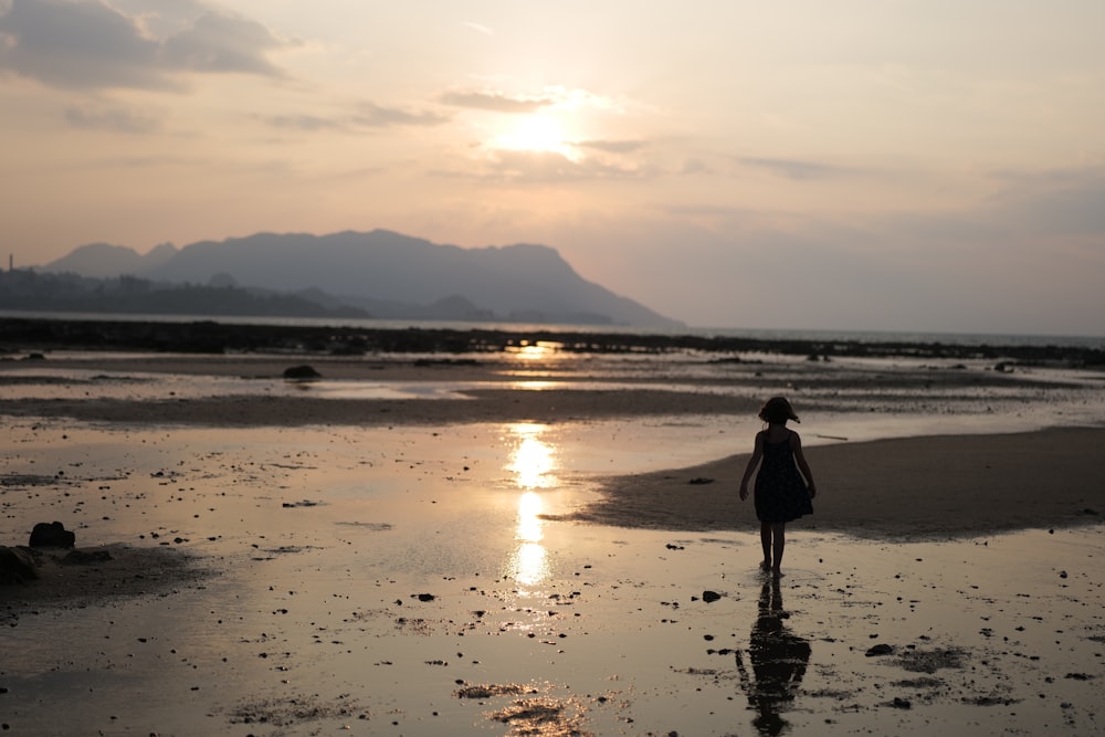 une personne marchant sur une plage au coucher du soleil