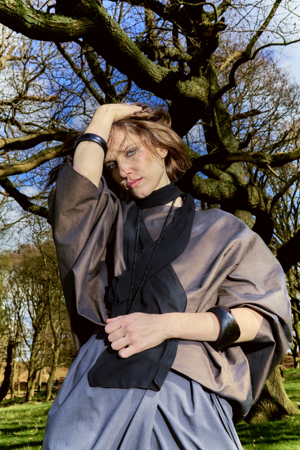 a woman standing in front of a tree with her hands on her head