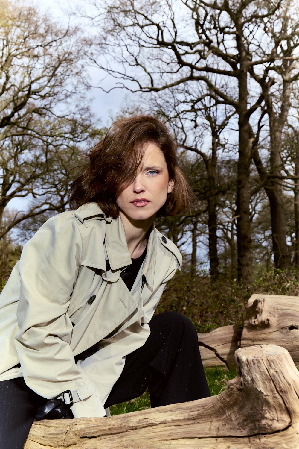 a woman in a trench coat sitting on a log
