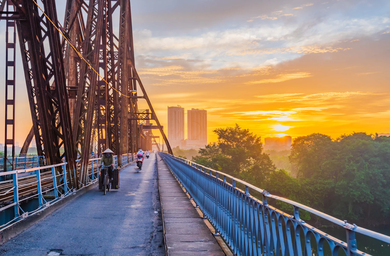 Golden sunrise over a long metal footbridge and a distant city skyline