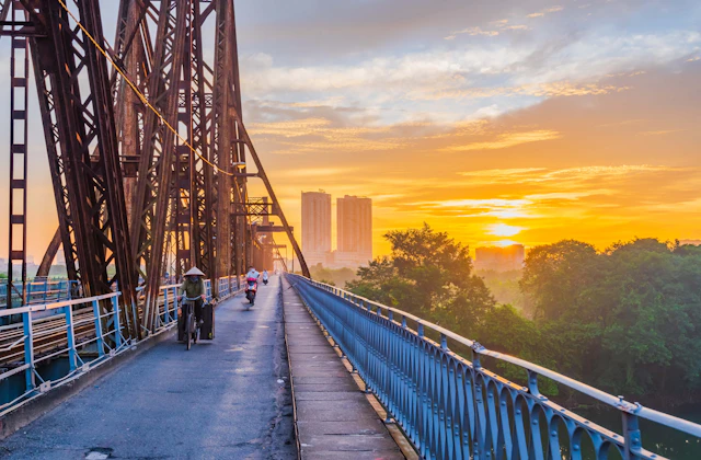 Golden sunrise over a long metal footbridge and a distant city skyline