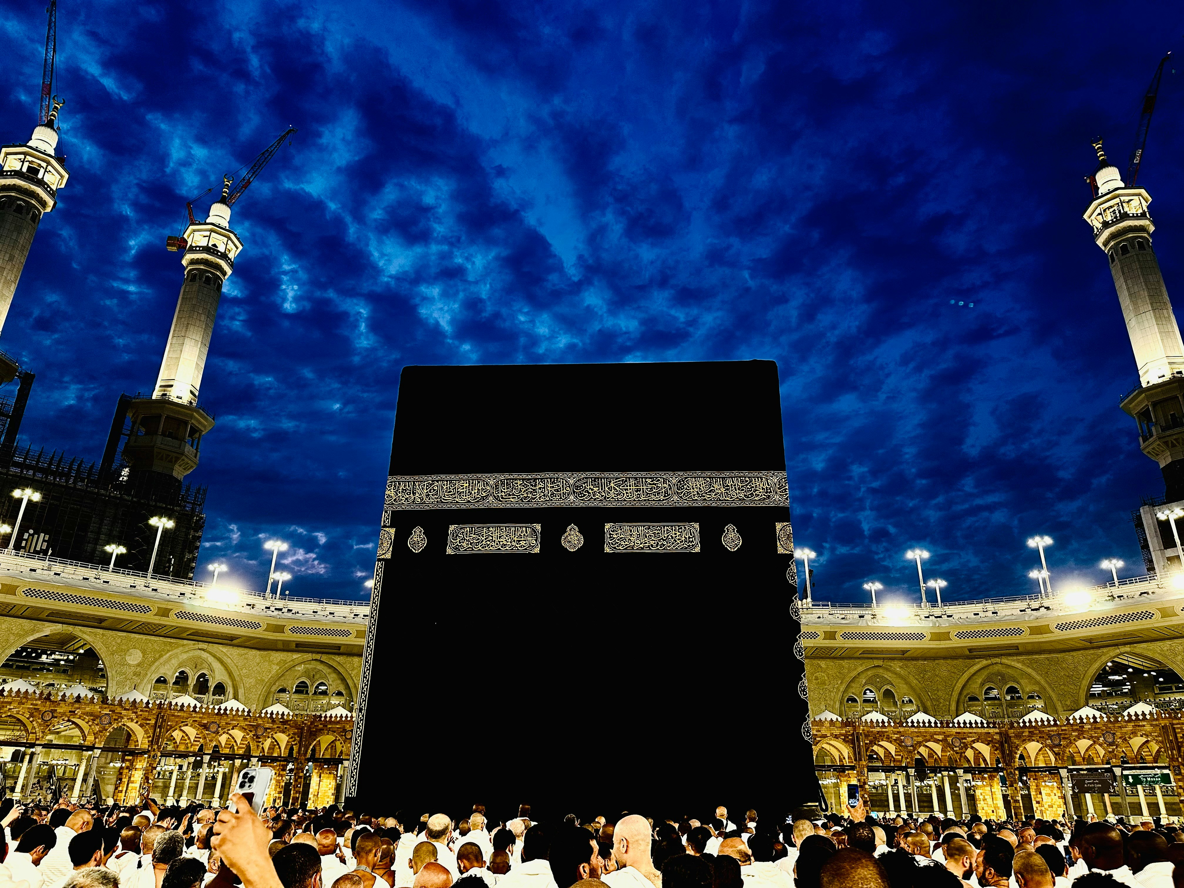 Aerial view of Masjid al-Haram with Kaaba, pilgrims performing tawaf, dramatic dark atmospheric sky, deep shadows