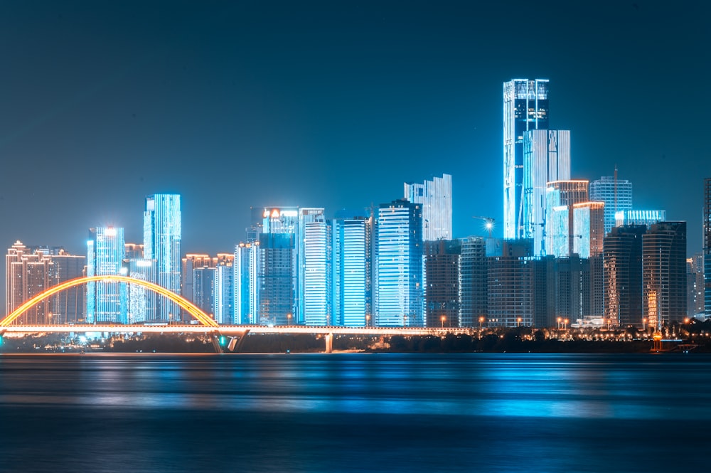 a city skyline at night with a bridge in the foreground
