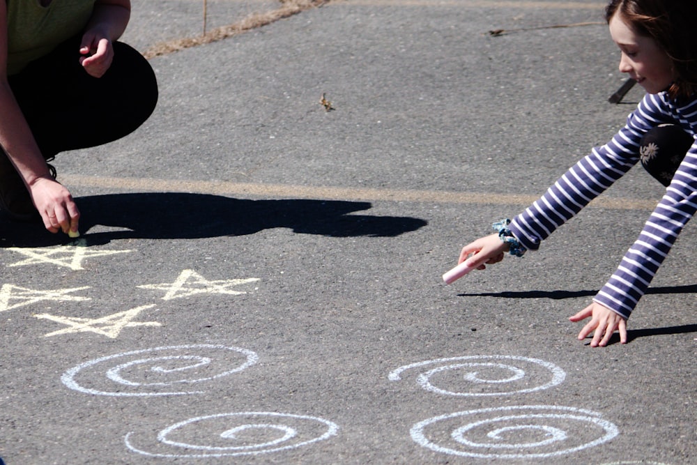 a young girl is drawing on the ground with chalk