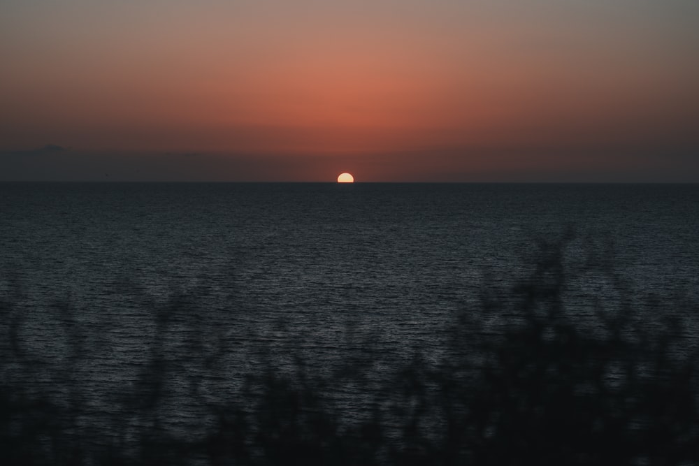 the sun is setting over the ocean as seen from a hill