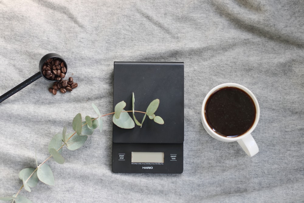 a scale, a cup of coffee and a spoon on a bed