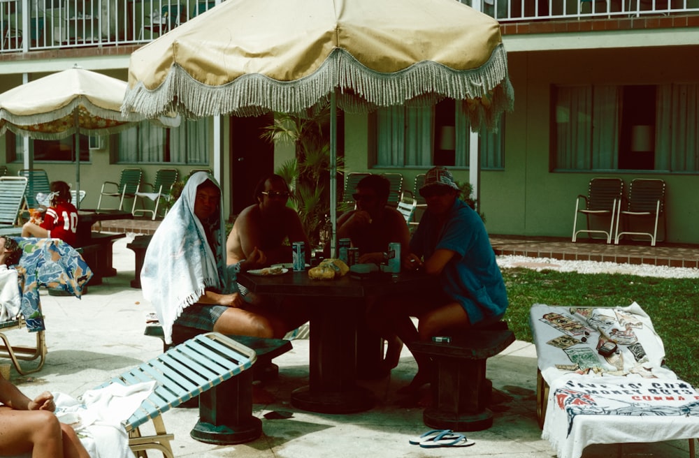 a group of people sitting around a table under an umbrella