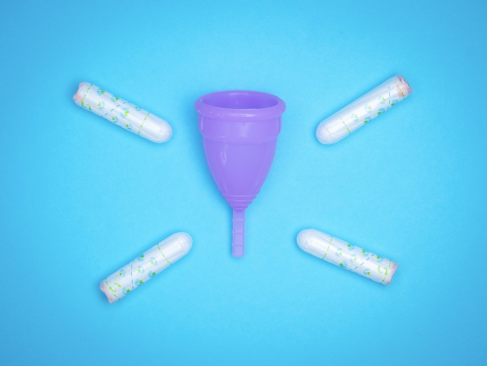 a purple plastic cup surrounded by five white pills