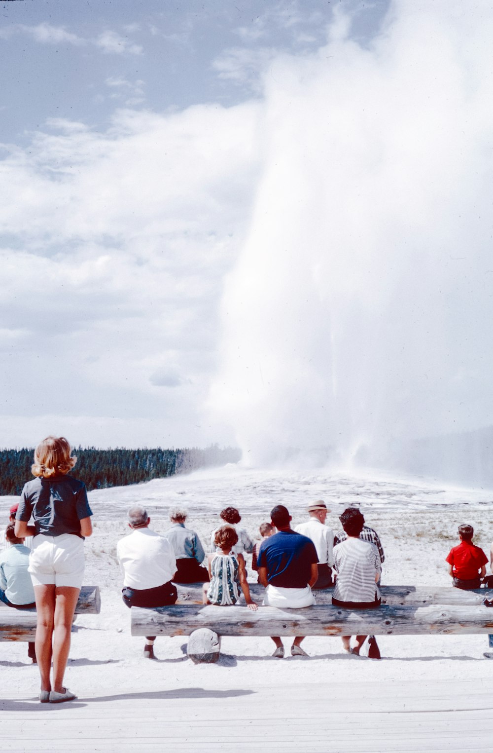a group of people sitting on a bench near a geyser