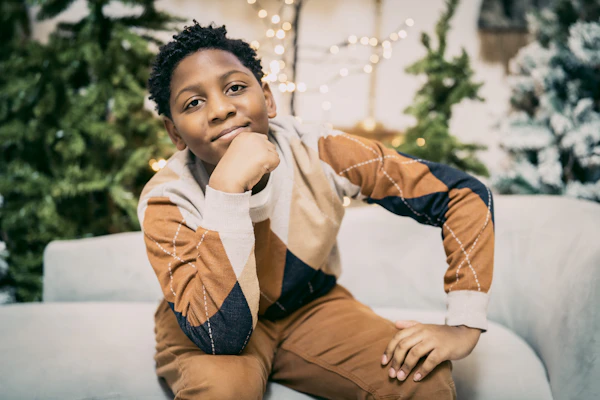 Boy in a holiday sweater posing by a Christmas tree