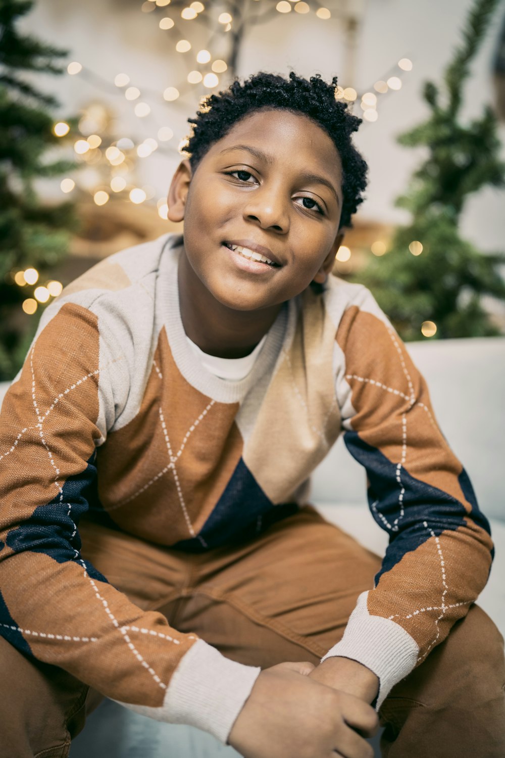 a young boy sitting on a couch in front of a christmas tree