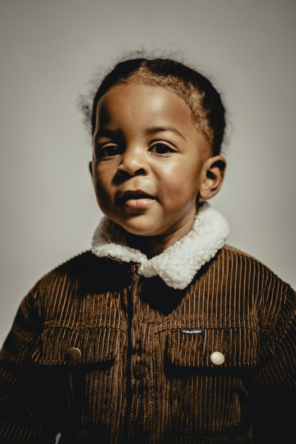 a small child with a brown jacket and a white collar