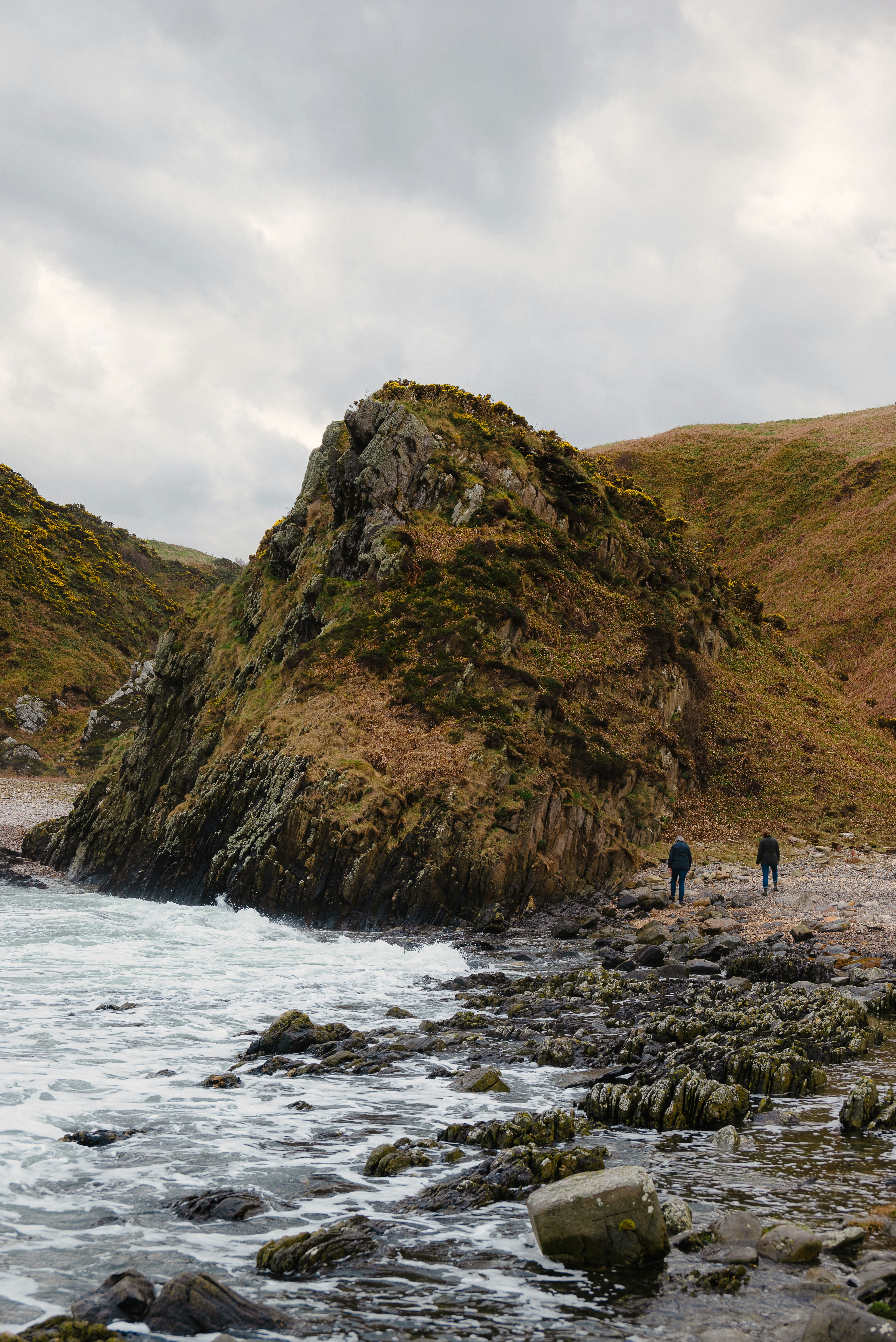 a couple of people walking along a rocky beach