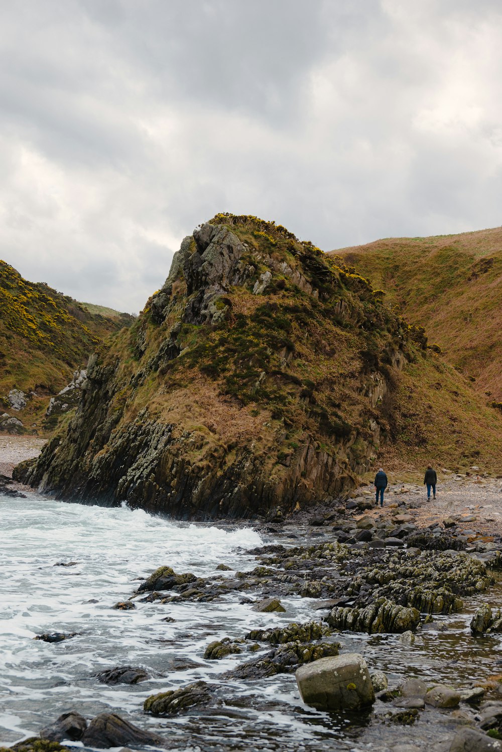 a couple of people walking along a rocky beach