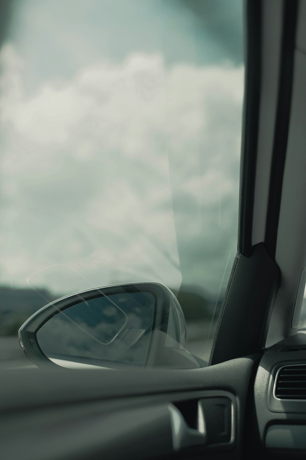 a side view mirror of a car with a cloudy sky in the background