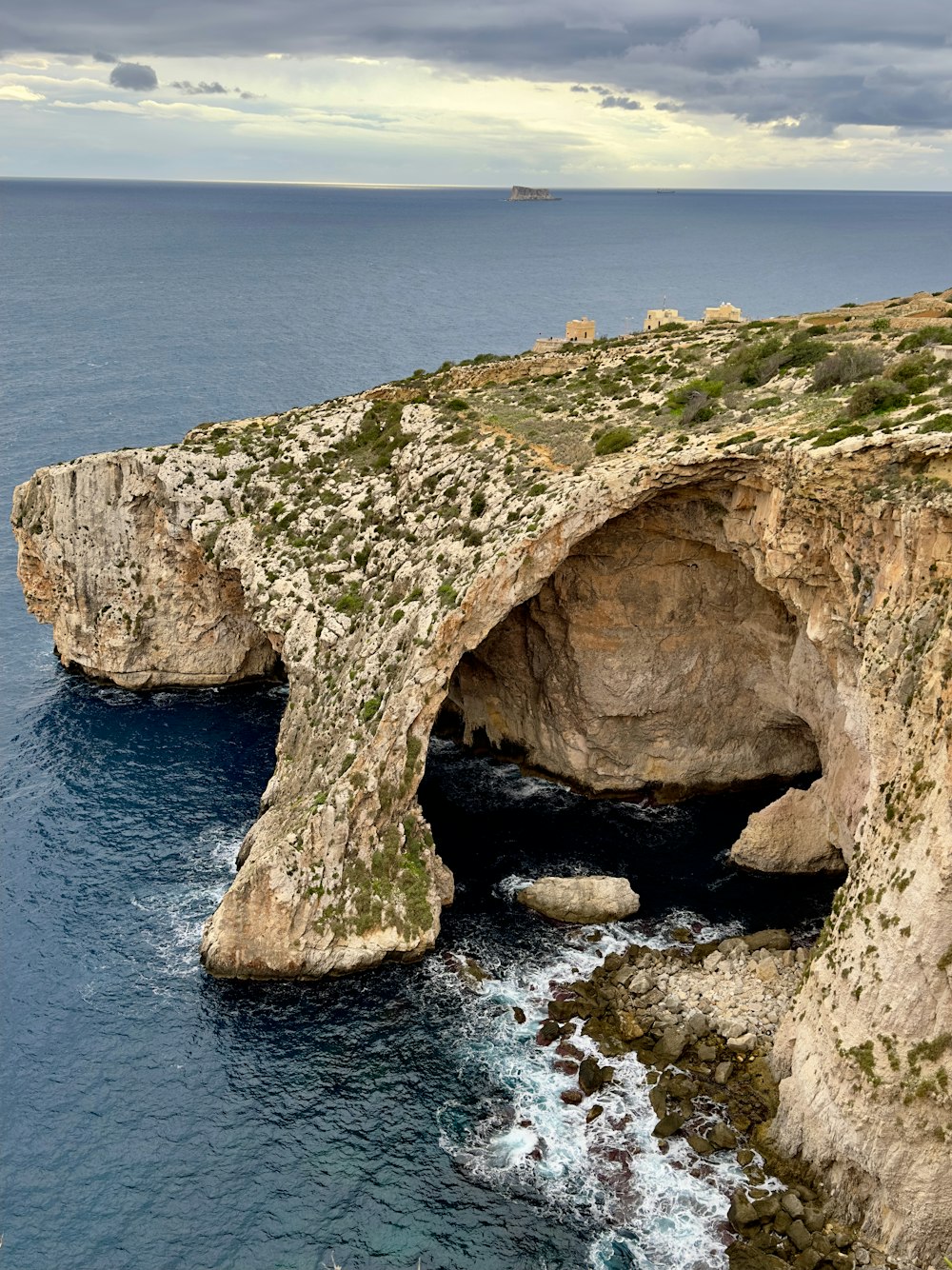 a large rock formation near the ocean under a cloudy sky