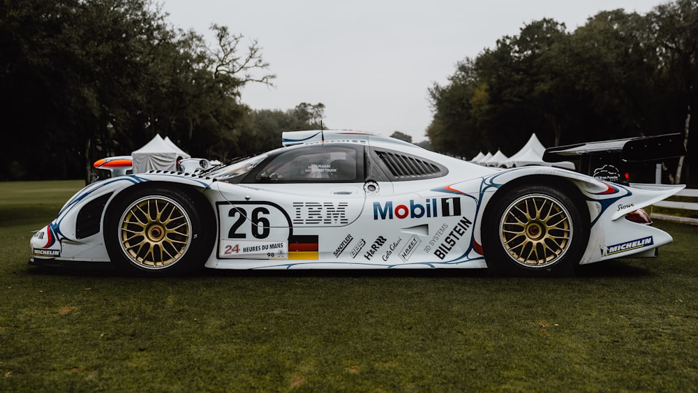 a white race car parked on top of a lush green field