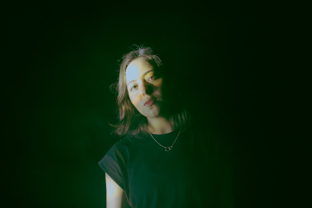 a woman standing in the dark with a necklace on