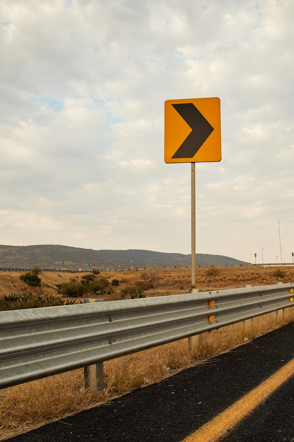 a yellow and black arrow sign sitting on the side of a road