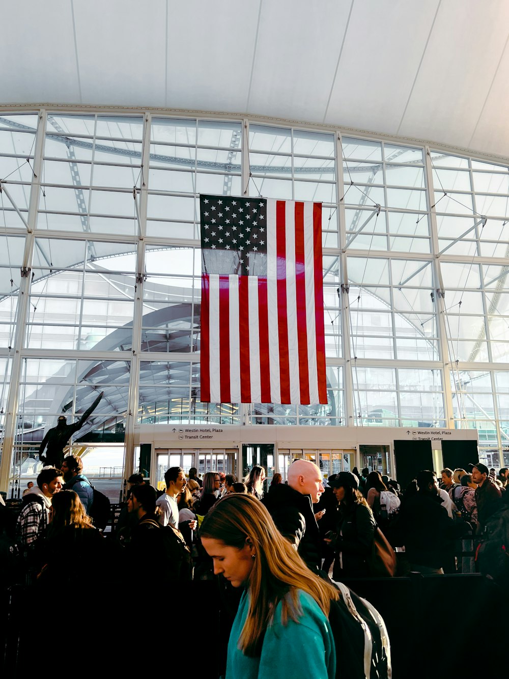 a crowd of people standing around a building with an american flag hanging from the ceiling