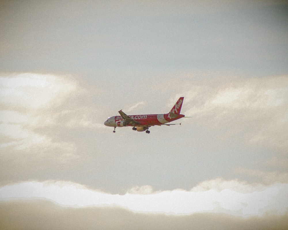 a red and white airplane flying through a cloudy sky