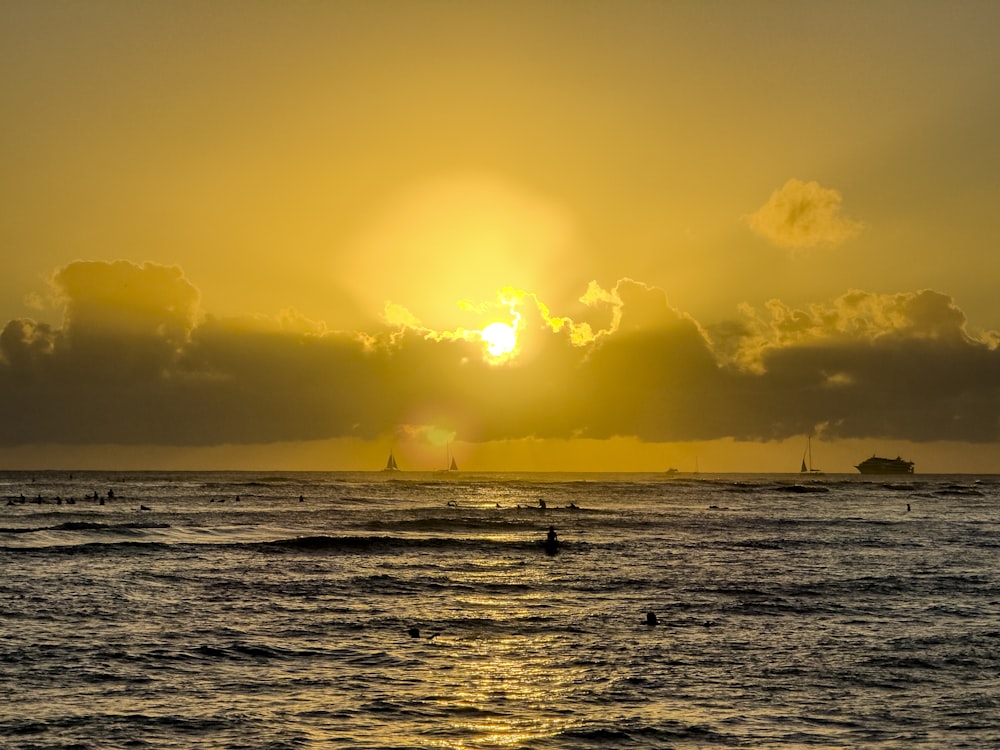 the sun is setting over the ocean with surfers in the water