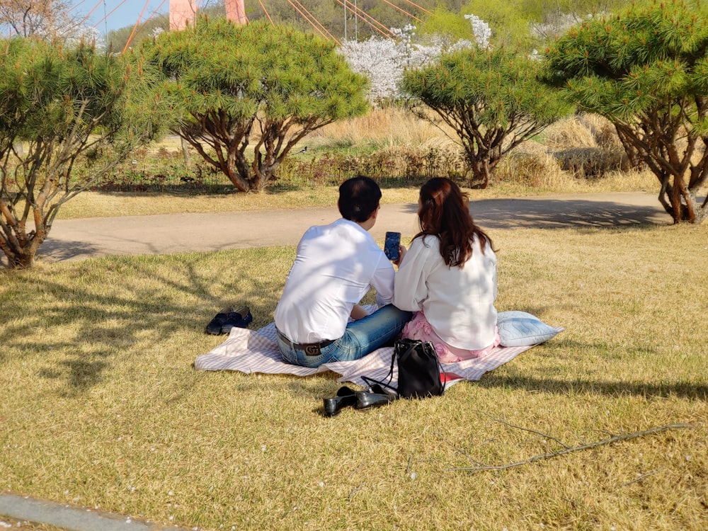 a man and a woman sitting on a blanket in a park
