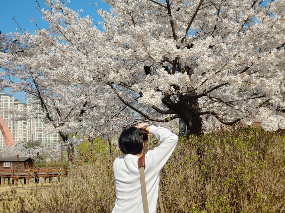 a woman is taking a picture of a cherry blossom tree