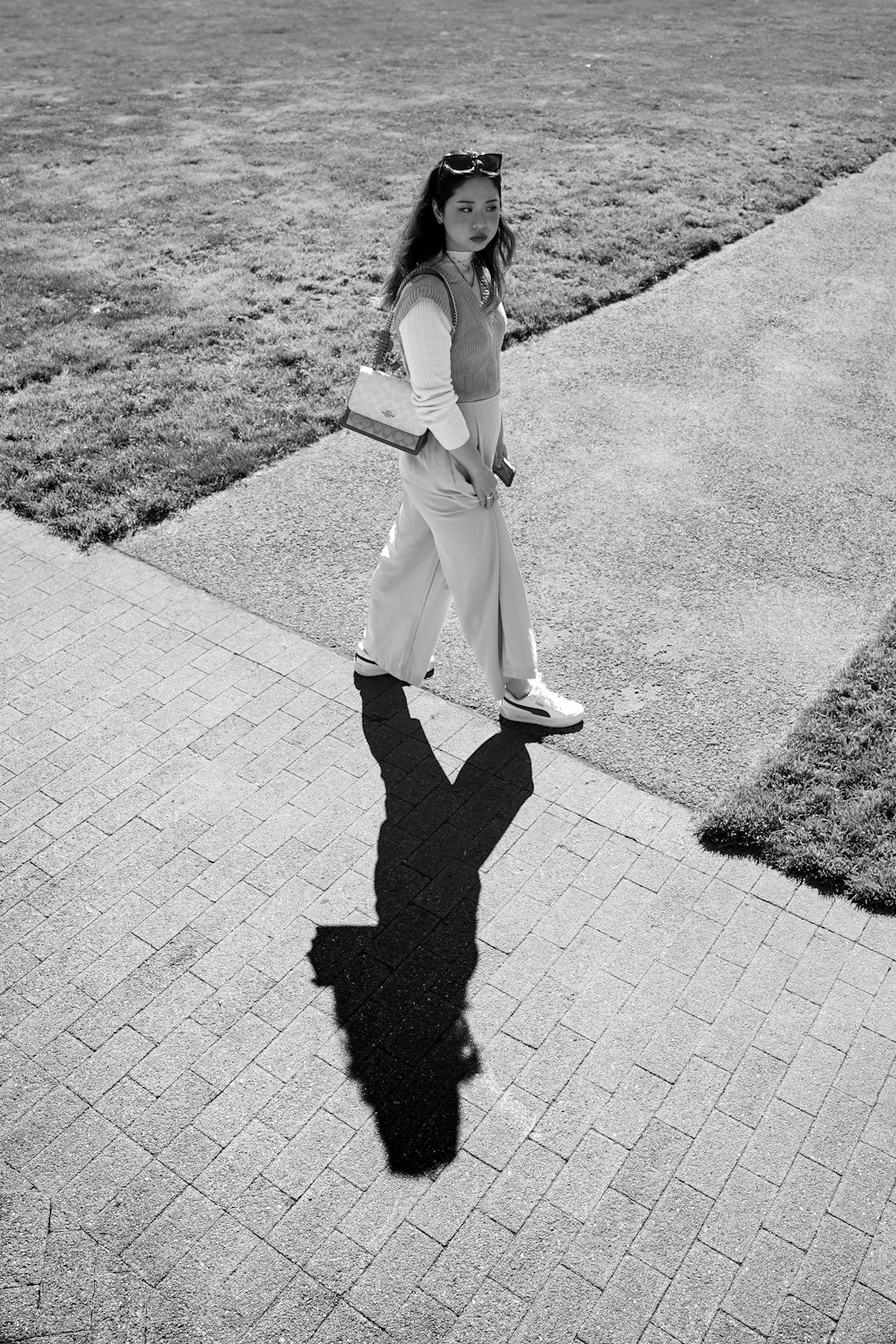 a woman walking down a sidewalk next to a grass covered field