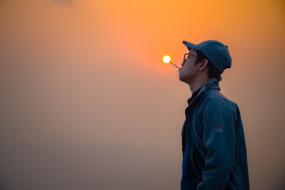 a man with a cigarette in his mouth standing in front of the sun