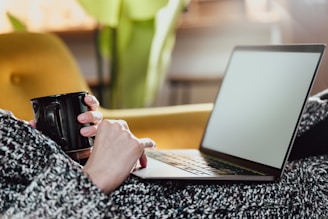 a woman holding a coffee mug while using a laptop