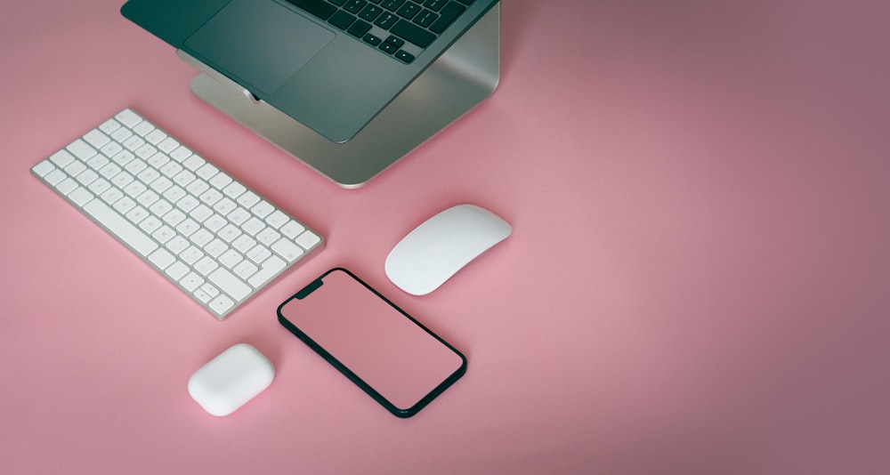 un teclado de computadora, un mouse y un teléfono celular sobre una superficie rosada