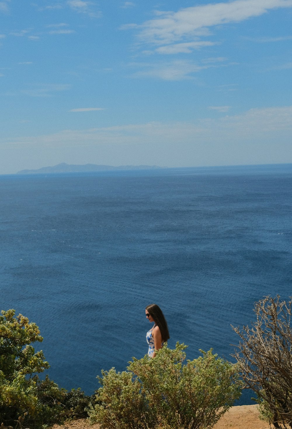 a woman standing on top of a hill next to the ocean