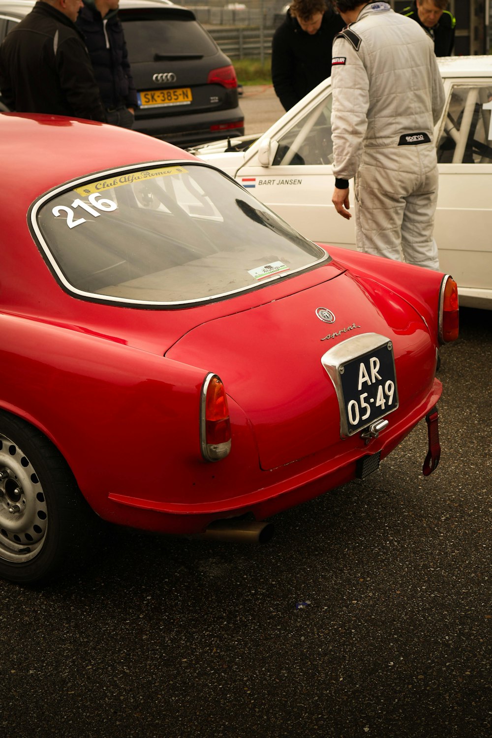 a group of people standing around a red car