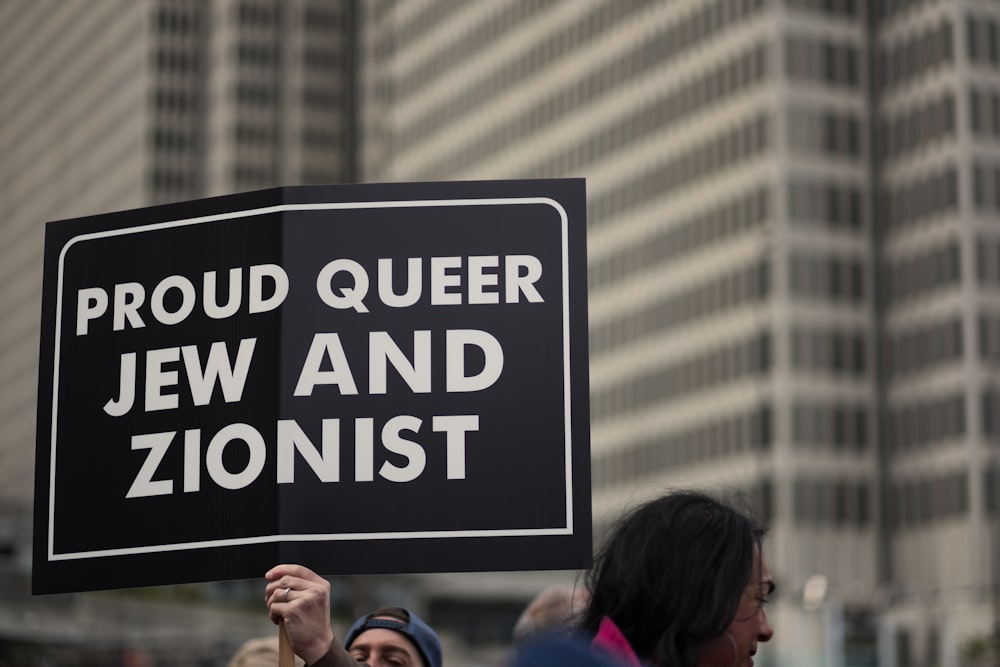 a person holding a sign that says proud queen jew and zoniist