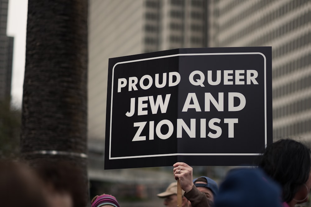 a person holding a sign that says proud queen jew and zoniist