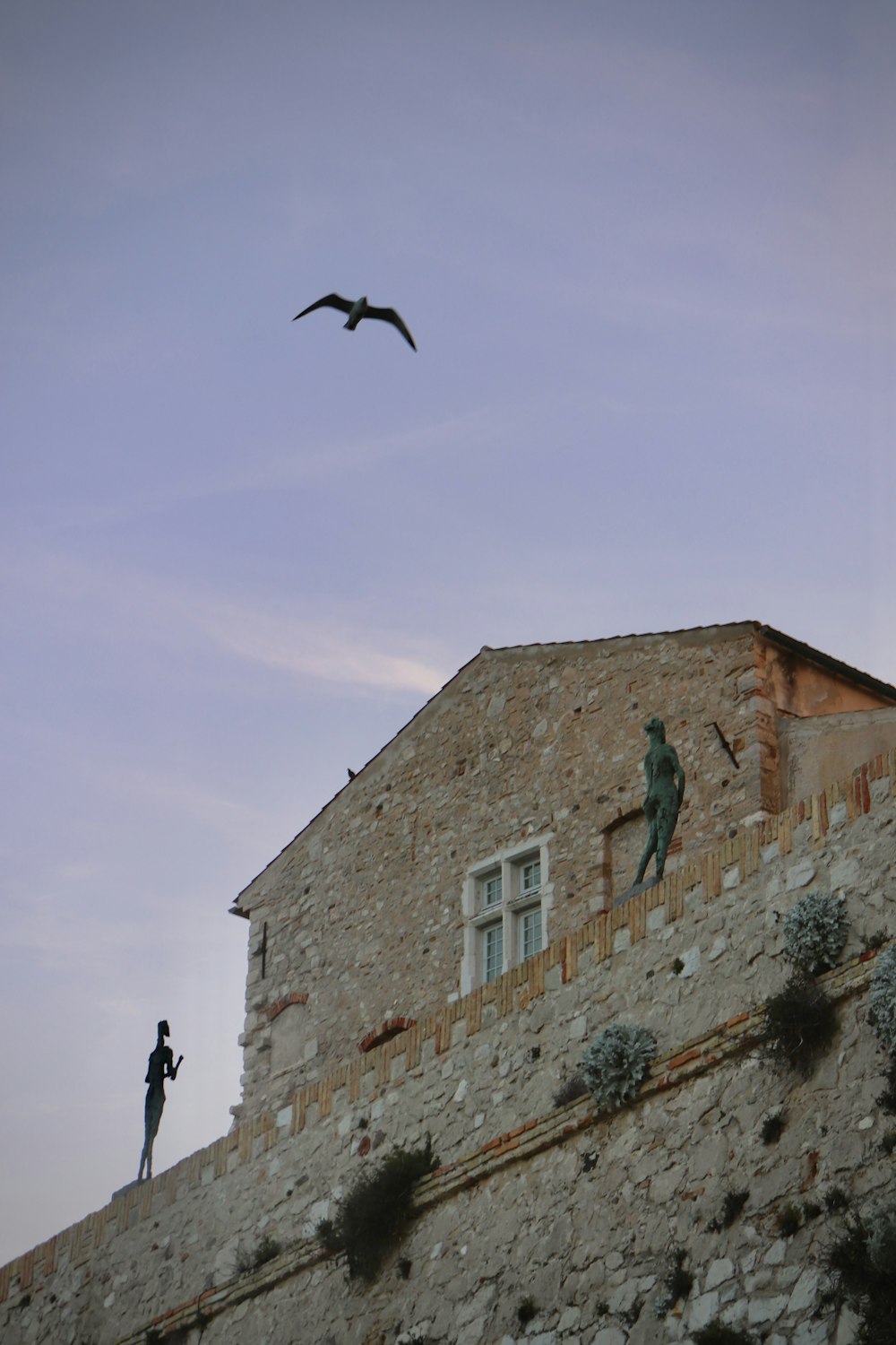 a bird flying over a building with a statue on it