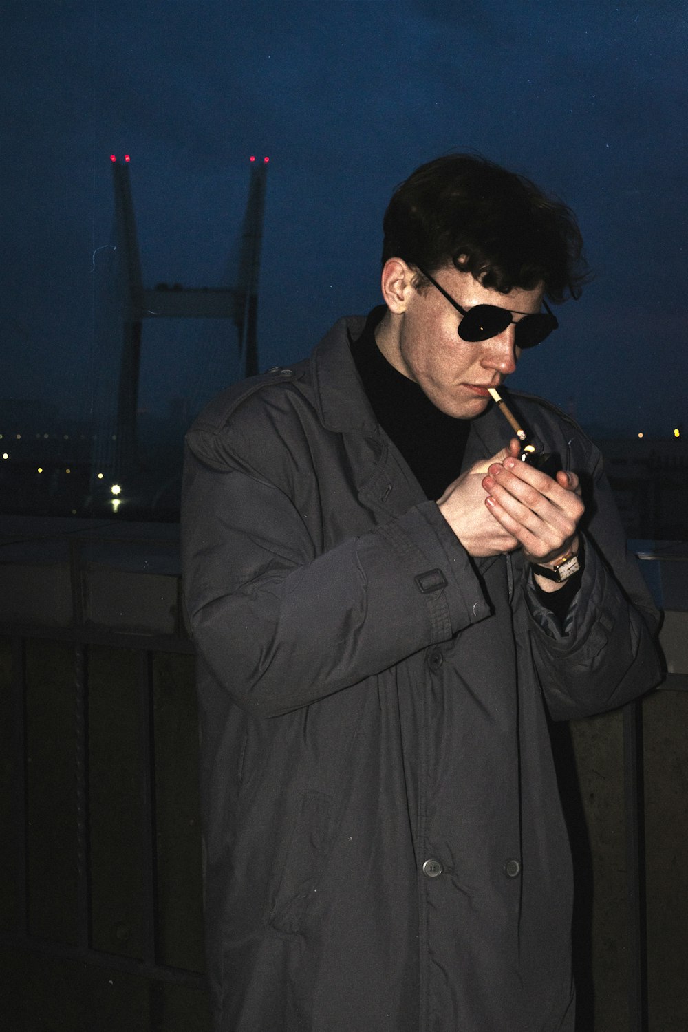 a man smoking a cigarette in front of a bridge