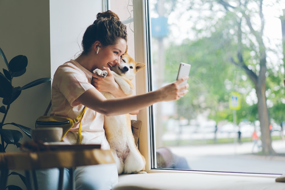 eine Frau, die auf ihr Handy schaut, während sie einen Hund hält