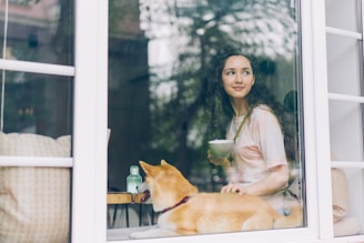 a woman sitting at a window with a dog