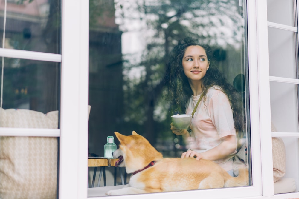 a woman sitting at a window with a dog