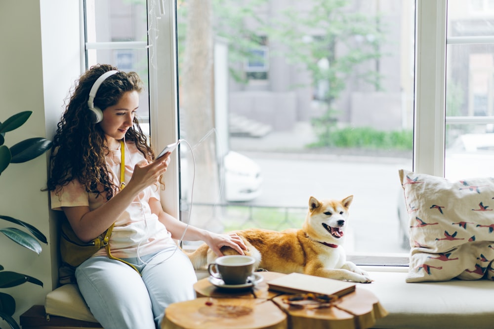 a woman sitting on a window sill next to a dog