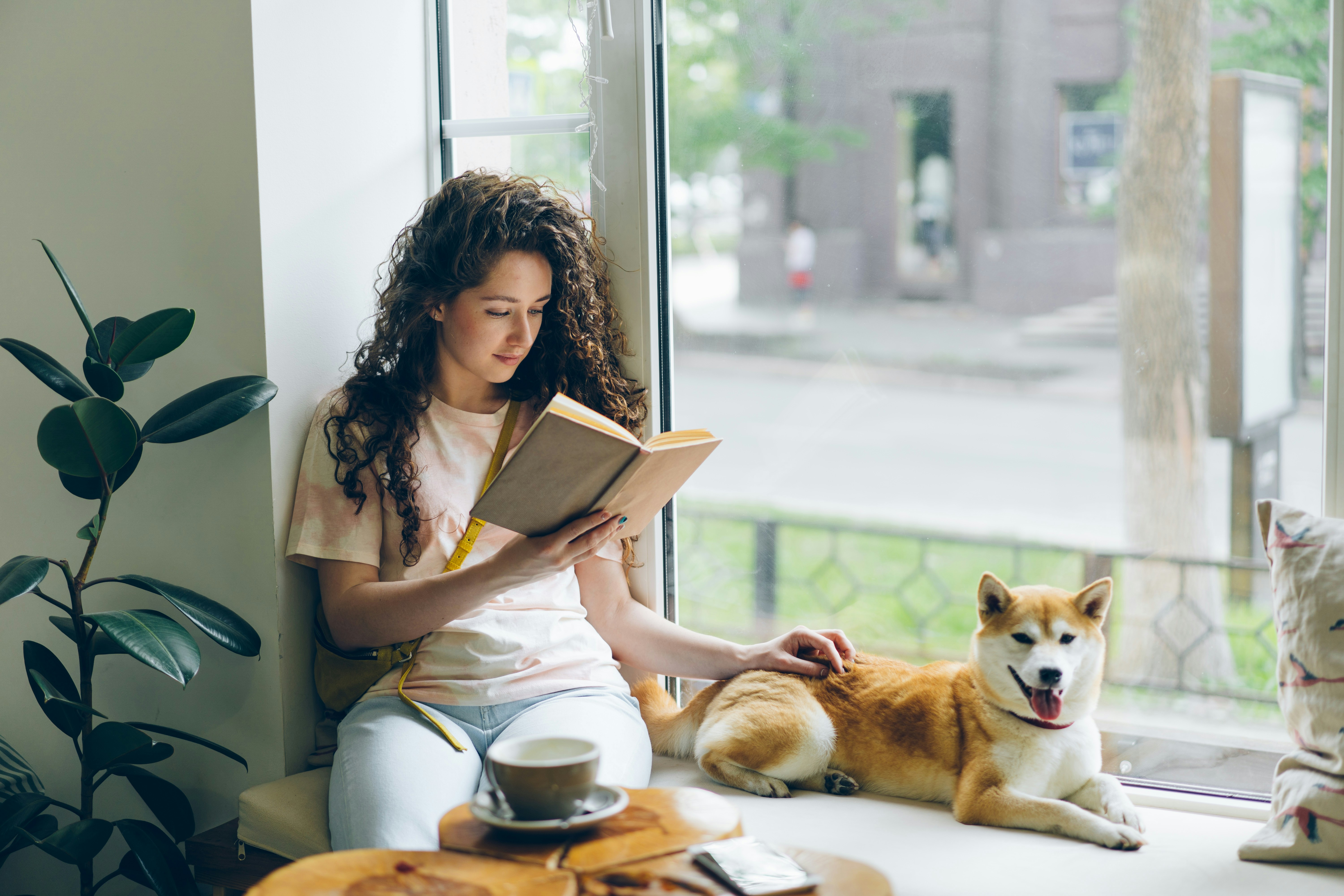 Female student reading with dog on window sill