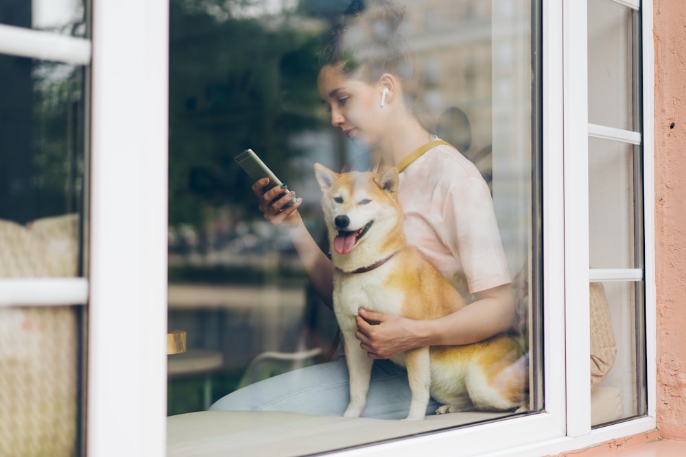 a woman sitting on a window sill holding a dog